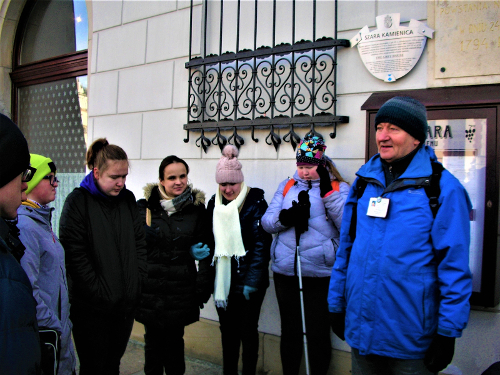 Fotografia: Uczestnicy wycieczki z przewodnikiem przed Szarą Kamienicą; jak głosi tablica: W domu tym mieściła się gł&oacute;wna kwatera Tadeusza Kościuszki i jego sztabu po wiekopomnym zaprzysiężeniu powstania narodowego w dniu 24 marca 1794 roku.